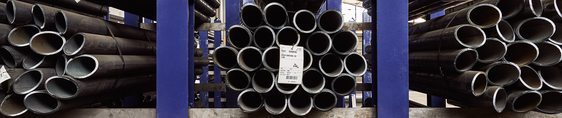 Stapel von Metallrohren in einem Lagerhaus, ordentlich auf blauen Regalen angeordnet, mit einem Etikett am mittleren Bündel.